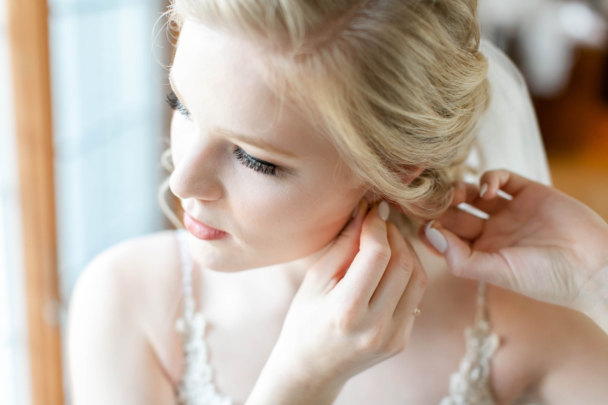 Close up of bride looking out window and putting on earring